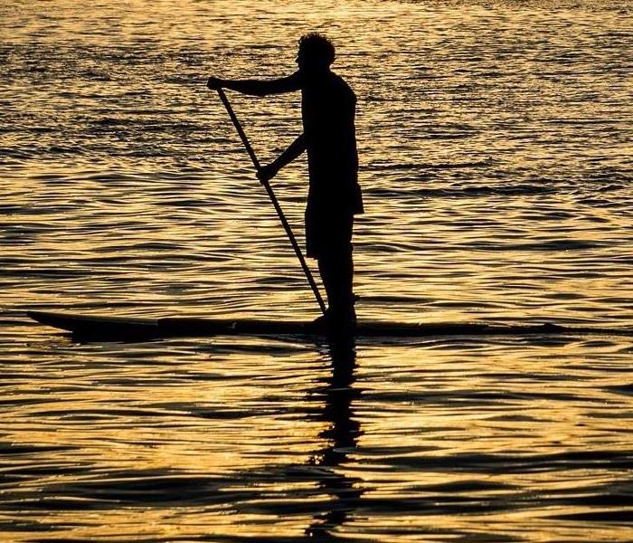 man on a paddle board paddling across a calm lake as the sun goes down