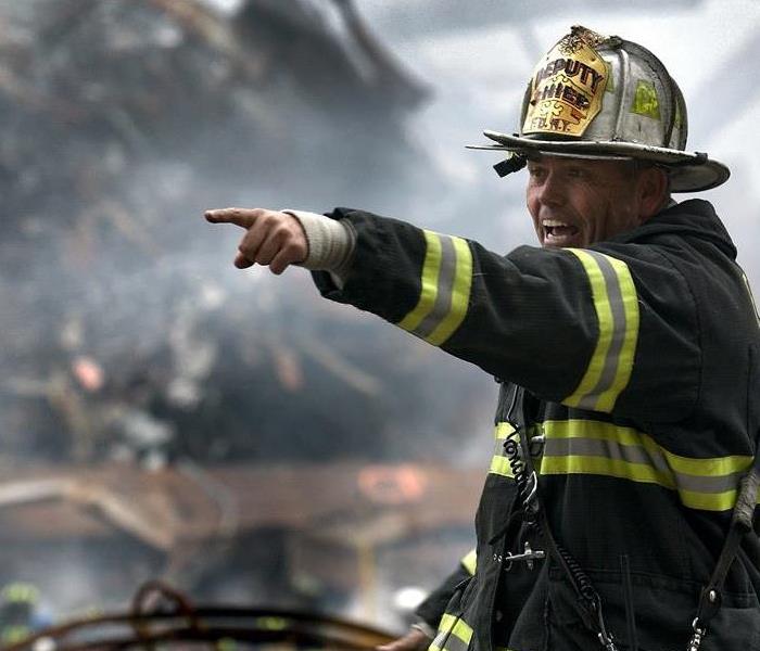 fireman pointing to the left in front of a background filled with large debris 