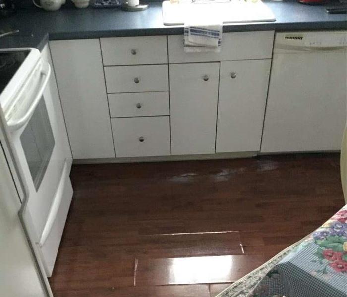 Standing water in kitchen next to white kitchen cabinets, with oven and sink